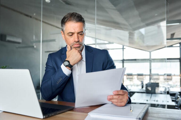 Man in a suit reviewing cybersecurity and IT documentation at his desk.