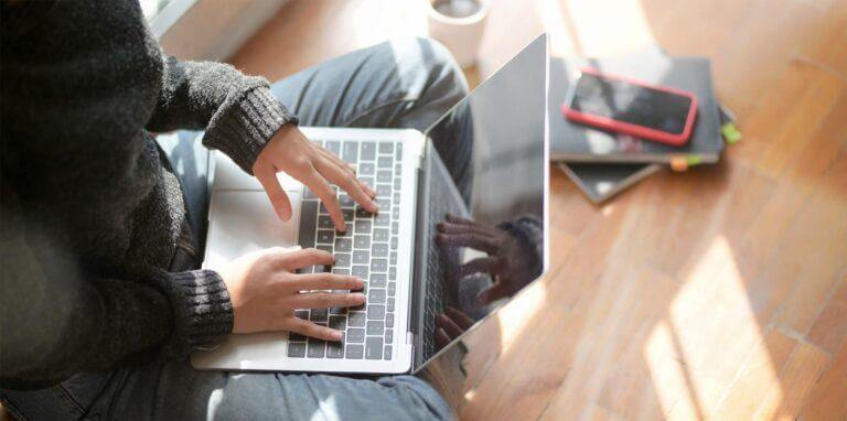 Employee sitting on the floor working from home on a laptop.