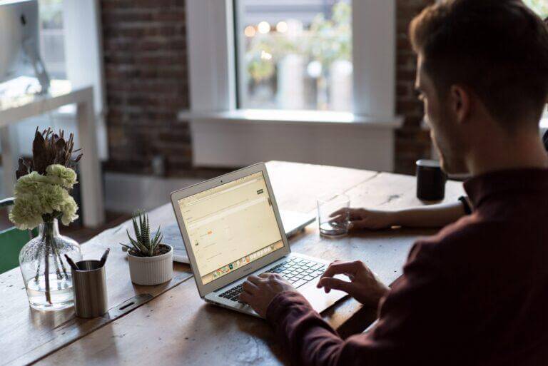 Young man sitting at a computer at a wood desk.
