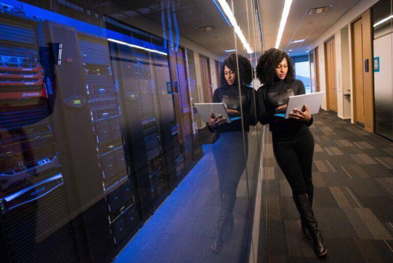 Female IT staff on a laptop outside an IT/server room.