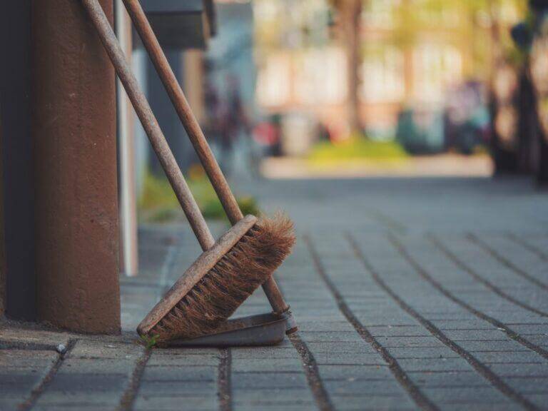 Broom and pan leaning against a building wall outside.