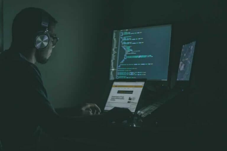 IT employee with headphones on working on laptop and reviewing code.