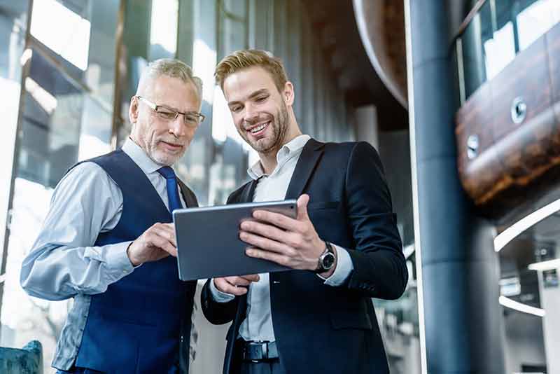 Two men looking at a tablet and talking, appearing engaged in discussion